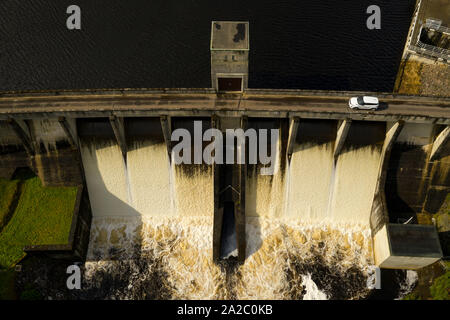 Wasser über die Meig Hydro Electric Damm in Highland Schottland fließen, mit einem Land Rover Evoque Auto fahren über die öffentliche Straße über die Staumauer. Stockfoto