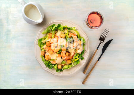 Garnelen Caesar Salat mit Parmesan Käse, Croutons und Salat, mit einem Glas Rose Wein und eine Sauciere Stockfoto