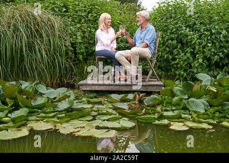Reifes Paar feiern mit Champagner Sitzen auf Stühlen auf hölzernen Steg am See Stockfoto
