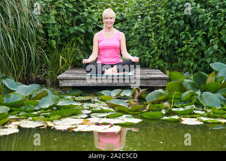 Portrait von reife Frau in Yoga Position auf hölzernen Steg am See Stockfoto