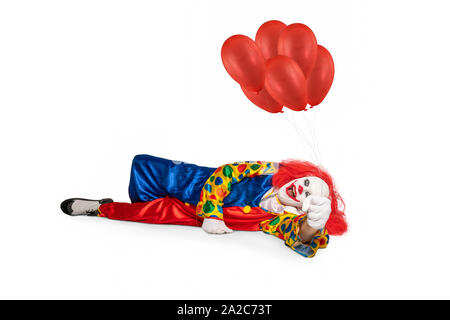 Fröhliche Clown auf dem Boden liegt, die Luftballons in der Hand Stockfoto