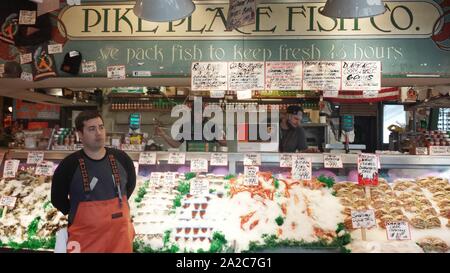 Fischhändler mit orangefarbenen Overalls stehen vor der Pike Place Fish Company auf dem Pike Place Market in Seattle, Washington, 21. April 2015. () Stockfoto