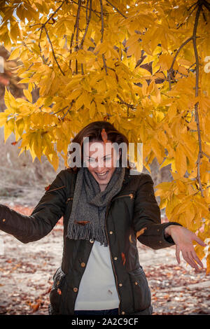 Schöne junge Frau in einem herbstlichen Wald werfen getrocknete orange Blätter und lachen Stockfoto