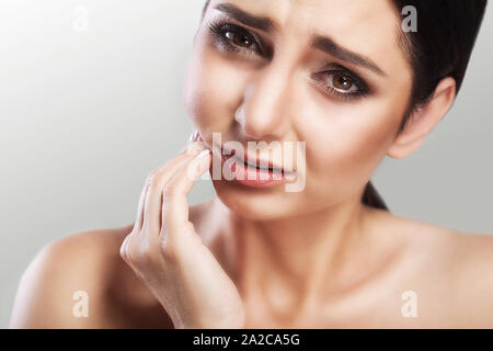 Stomatologie der Hilfe- und Zahnschmerzen. Eine junge Frau lehrt, ein Mädchen, das von einem schrecklichen Schmerzen in den Zähnen leidet, ihre Handflächen berühren sich und ihre Wangen. Kears Stockfoto