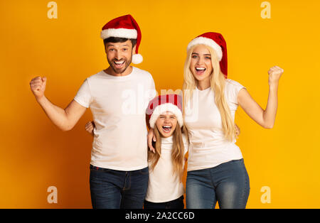 Aufgeregt Familie in Santa Hüte Schütteln Fäuste auf gelbem Hintergrund Stockfoto