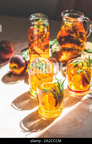 Gläser süßer Pfirsich Eistee, Sommer kalt Pfirsich fizz Cocktail mit Rosmarin. Sonnigen Licht. Geringe Tiefe des Feldes, Nahaufnahme, kopieren Sie Raum für Sie Stockfoto