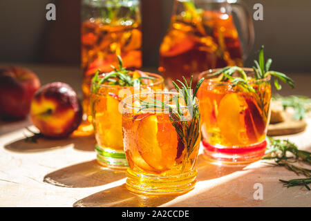 Gläser mit Tropfen süßen Pfirsich Eistee, Sommer kalt Pfirsich fizz Cocktail mit Rosmarin. Sonnigen Licht. Geringe Tiefe des Feldes, Nahaufnahme, kopieren Spa Stockfoto