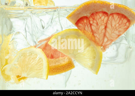 Nahaufnahme von Zitrone und Grapefruit Schichten in Limonade und Eiswürfel Hintergrund. Textur der Kühlung's Sweet Summer Drink mit Makro Blasen an der Glaswand. Zischenden oder schwimmend auf der Oberfläche nach oben. Stockfoto
