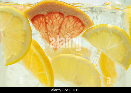 Nahaufnahme von Zitrone und Grapefruit Schichten in Limonade und Eiswürfel Hintergrund. Textur der Kühlung's Sweet Summer Drink mit Makro Blasen an der Glaswand. Zischenden oder schwimmend auf der Oberfläche nach oben. Stockfoto