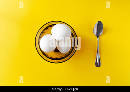 Flach der weiße Eier in eine Schüssel und Löffel in der Nähe von Es auf gelben Hintergrund. Internationale Welt ei Tag Konzept Stockfoto