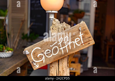 Board auf einem hölzernen Pfosten vor einem Geschäft mit dem Wort "geoeffnet" - das ist Deutsch für 'Öffnen'. Stockfoto