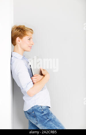 Attraktive junge Frau hält einen Laptop-Computer gleichzeitig an eine Wand gelehnt. Stockfoto