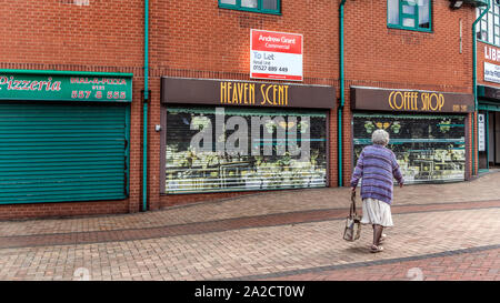 Ältere Frau vorbei geschlossen, die Geschäfte in der Fußgängerzone von Tipton, nordwestlich von Birmingham, West Midlands, UK Mit einem commerial Eigenschaft Zeichen im Hintergrund lassen. Stockfoto