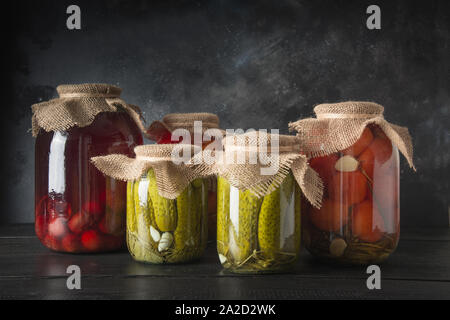 Konserven fermentierten Früchte und Gemüse, Pflaume, Gurke, Tomate, die in Gläsern auf dunklen Holz- Board. Verschiedene Arten von Fermentiert. Horizontale Ausrichtung. Stockfoto