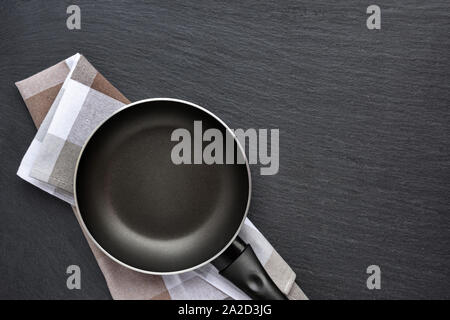 Leere Pfanne mit Küchentuch auf dunklen grauen Stein Hintergrund. Ansicht von oben Stockfoto