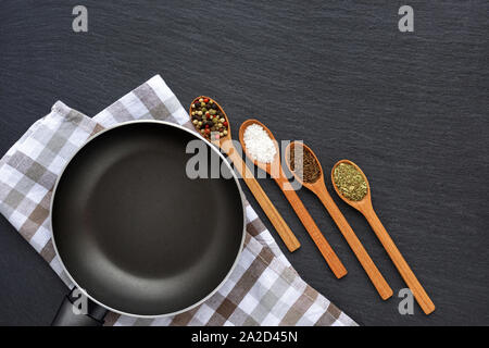 Leere Pfanne mit Serviette und Gewürzen auf dunklen grauen Stein Hintergrund. Ansicht von oben Stockfoto