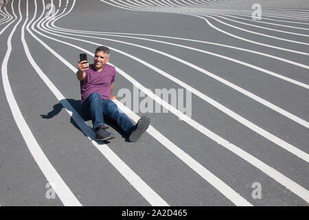 Lächelnde grauhaarige Mann macht einen selfie sitzen auf dem Boden. Stockfoto