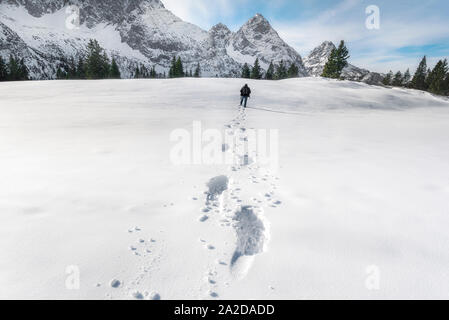 Mann zu Fuß durch Schnee, verschneite Berggipfel und Tannen. Spuren im Schnee. Fuß Spuren im Schnee. Winterlandschaft. Stockfoto