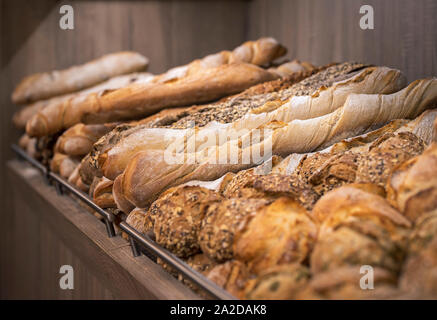 Brotmischung auf hölzernen Regalen. Backwaren auf einem Regal angezeigt. Verschiedene Arten von Broten. Frisch gebackene knusprige Brot. Appetitlich französischem Brot. Stockfoto