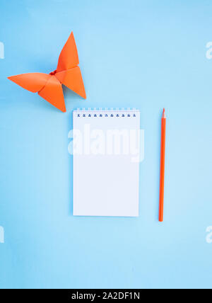 Eine Bleistifte, ein Notebook und ein Papier Schmetterling auf blauem Hintergrund mit Copyspace. Flach Stil. Zurück zum Konzept der Schule. Stockfoto