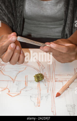 Junge Frau das Rollen einer gemeinsamen von Marihuana während einer Pause nach Zeichnung. Konzept von Drogen in der Art Hintergrund mit Cannabis bud, Bleistifte und Skizzen Stockfoto