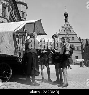 Eine Marktfrau Drucken drei Hitlerjungen Obst von Ihrem mit dem Markt stehen in Rothenburg o.d. Tauber, Deutschland 1930er Jahre. Drei Hitler Jugend sind einige Früchte aus einer Marktfrau in Rothenburg o.d. Tauber, Deutschland 1930 s angegeben. Stockfoto