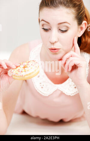 Junge Frau entscheiden, ob Sie eine ungesunde Donut mit dem Ausdruck ihrer Schuld zu essen. Stockfoto