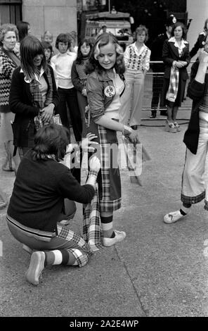 70er Jahre UK Teenage Mädchen Bay City Roller Fans Last Minute Anpassungen an Tartan Mode der Zeit. Vor Rollers Konzert im Hammersmith Odeon, West London 1975. HOMER SYKES Stockfoto