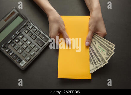 Konzept der Gehalt oder bestechungsgeld für die Arbeit. Gelber Umschlag mit Geld auf einem dunklen Tisch. Stockfoto