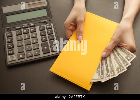 Geschäft und Profit Konzept mit Rechner, Geld und weibliche Hände mit gelben Umschlag. Stockfoto