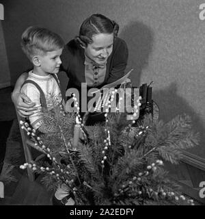 Ein kleiner Junge schreibt-Wunschzettel an den Weihnachtsmann mit der Schreibmaschine und gibt ihn seiner Mutter zur Weiterleitung, Deutschland 1930er Jahre. Ein kleiner Junge mit der Eingabe seiner Liste der Wünsche und gibt ihm seine Mutter zur Weiterleitung an Santa, Deutschland 1930. Stockfoto