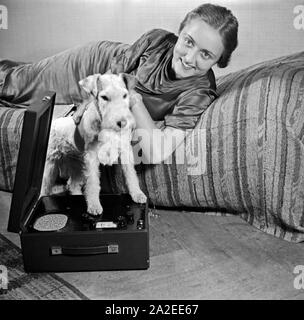 Eine Dame mit Hund und Nora Olympia Kofferradio im Fotostudio in zeitgenössischer Mode, Deutschland 1930er Jahre. Eine Frau und ihr Hund Haustier auf dem Foto Studio in der zeitgenössischen Mode, Deutschland 1930. Stockfoto