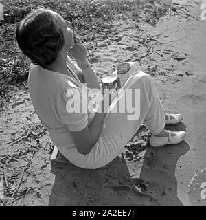 Einen guten Schutz gegen Sonnenbrand bietet Nivea Creme, eine junge Frau am Ufer eines sieht, Deutschland 1930er Jahre. Eine Nivea Creme schützt der Sonnenbrand, junge Frau Aufrahmen, Deutschland 1930. Stockfoto
