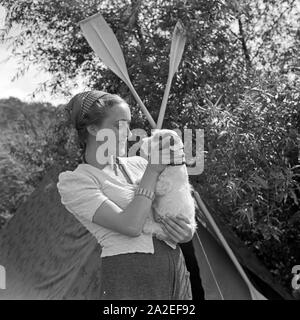 Werbefoto für Klepper Zelt: Getreu dem Werbeslogan Fahre fröhlich in die weite Welt, mit Klepper-Mantel,-Boot-und-Zelt spielt eine junge Frau mit einem Welpen vor einem Zelt, Deutschland 1930er Jahre. Werbung für ein Klepper Zelt: Eine junge Frau spielt mit einem Hund vor einem Zelt, Deutschland 1930. Stockfoto