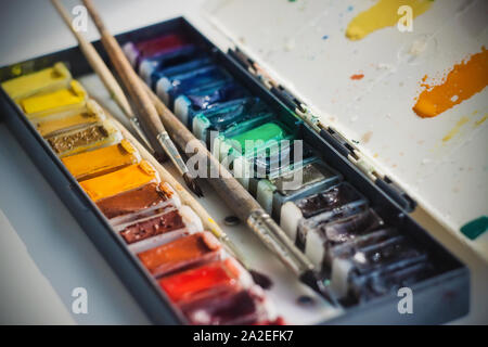 Vier Bürsten in verschiedenen Größen sind in einer Plastikbox mit Wasserfarben in vielen Schattierungen. Das Kontrollkästchen kann auch als Palette verwendet werden. Stockfoto
