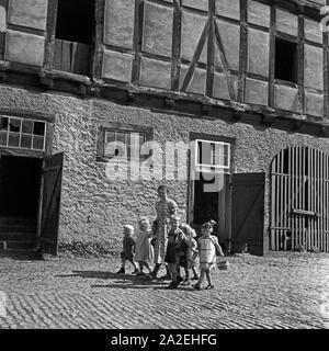 Ein Mädchen paßt auf kleine Kinder mit im Rahmen ihres Aufenthalts im Mädel Landjahr in Polle an der Weser und spaziert mit ihnen ein einem alten Bauernhof vorbei, Deutschland 1930er Jahre. Ein Mädchen Baby- manche Kinder während der BdM-Camp in Polle und Bummeln, neben einem Bauernhof, Deutschland 1930. Stockfoto