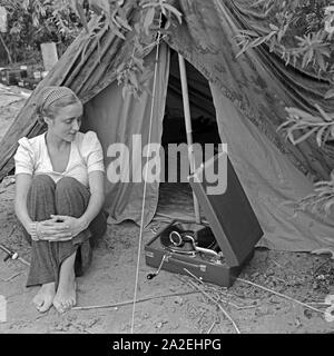 Werbefoto für Klepper Zelt: Getreu dem Werbeslogan Fahre fröhlich in die weite Welt, mit Klepper-Mantel,-Boot-und-Zelt sitzt eine junge Frau mit einem grammophon vor einem Zelt, Deutschland 1930er Jahre. Werbung für ein Klepper Zelt: Eine junge Frau sitzt mit einem grammophon vor einem Zelt, Deutschland 1930. Stockfoto