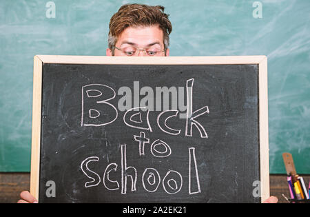 Lehrer oder Schulleiter begrüßt Inschrift zurück in die Schule. Lehrer heraus spähen Tafel. Erzieher versteckt sich hinter Tafel. Bildungschancen. Schuljahr vorbereiten. Sind Sie bereit, zu studieren. Stockfoto