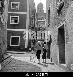 Zwei junge Frauen gehen mit dem Hund durch eine kleine Gasse in Passau in Richtung Stephansdom, Deutschland 1930er Jahre. Zwei Frauen und ihren Hund durch eine kleine Gasse von Passau in Richtung Stephansdom bummeln, Deutschland 1930. Stockfoto