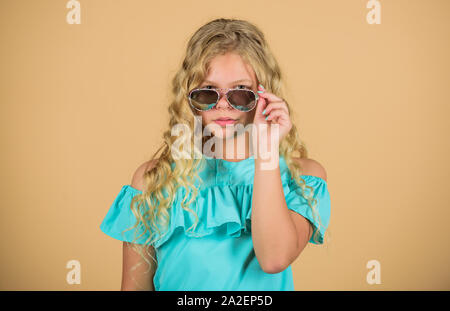 UV-Schutz. Die Gesundheit der Augen. Die richtige Sonnenbrille kaufen. Optik speichern. Süße kleine Kid Mode Mädchen. Mädchen langes lockiges Haar, tragen Sie eine Sonnenbrille. Sonnenbrille Sommer Zubehör. Sommer Trend. Wenig Fashionista. Stockfoto