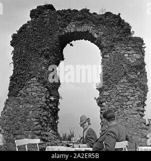 Ein Paar sitzt auf einer Terrasse vor dem Rolandsbogen in Rolandswerth, einem Stadtteil von Remagen, Deutschland 1930er Jahre. Ein paar sitzt auf einem Restaurant Terrasse vor der Rolandsbogen Rolandswerth arch in der Nähe von Remagen, Deutschland 1930. Stockfoto