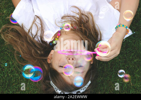 Blick von oben auf ein wunderschönes kleines Mädchen mit auf dem Gras, bläst Seifenblasen Stockfoto