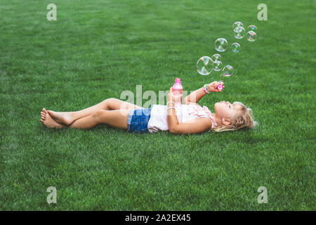 Kleines Mädchen mit auf dem Gras, bläst Seifenblasen Stockfoto