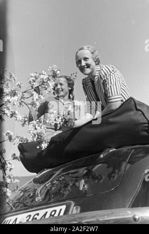 Zwei junge Frauen machen 5/6 einer Spazierfahrt mit dem Cabrio unter einem blühenden Kirschbaum im Schwarzwald Rast, Deutschland 1930er Jahre. Zwei junge Frauen ruhen unter einem blühenden Kirschbaum im Schwarzwald während Ihrer Reise mit einem Cabrio, Deutschland 1930. Stockfoto