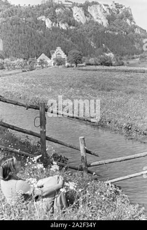 Eine Junge Frau Sitzt Im Gras Einer Wiese Vor Einem Kleinen Bach Im Schwarzwald, Deutschland, 1930er Jahre. Eine junge Frau sitzt an einem kleinen Bach im Schwarzwald, Deutschland der 1930er Jahre in die Gras. Stockfoto