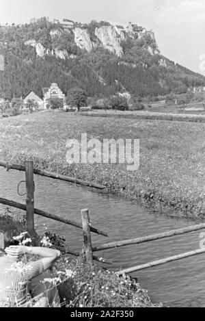 Eine Junge Frau Sitzt Im Gras Einer Wiese Vor Einem Kleinen Bach Im Schwarzwald, Deutschland, 1930er Jahre. Eine junge Frau sitzt an einem kleinen Bach im Schwarzwald, Deutschland der 1930er Jahre in die Gras. Stockfoto