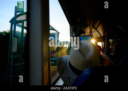 Der Bus Passagier Blick aus dem Fenster an der Bushaltestelle hinter einem Passagier trägt einen Stetson style Strohhut Stockfoto