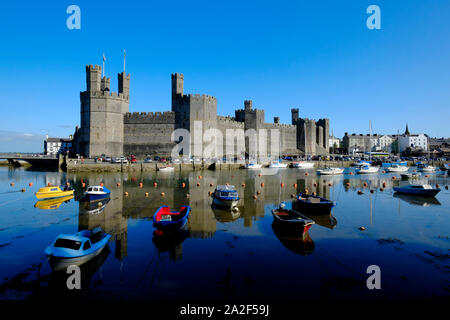 Blick über den Fluss Sieont auf Caernarfon Castle auf einem noch ruhig am Morgen auf dem Wasser widerspiegeln, bei Flut mit angelegten Boote im Vordergrund. Stockfoto