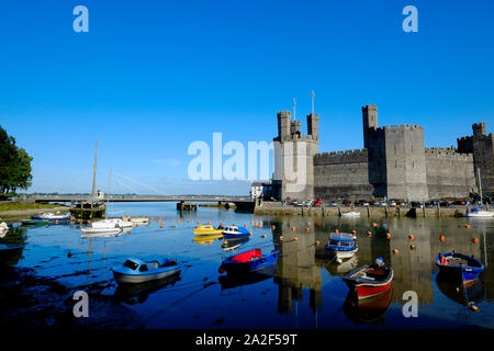 Blick über den Fluss Sieont auf Caernarfon Castle auf einem noch ruhig am Morgen auf dem Wasser widerspiegeln, bei Flut mit angelegten Boote im Vordergrund. Stockfoto