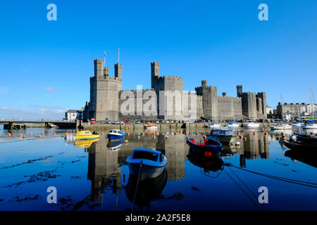 Blick über den Fluss Sieont auf Caernarfon Castle auf einem noch ruhig am Morgen auf dem Wasser widerspiegeln, bei Flut mit angelegten Boote im Vordergrund. Stockfoto